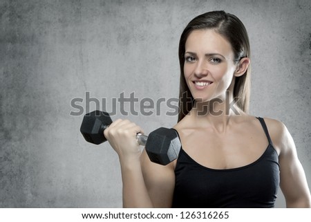 Beautiful sporty muscular woman with a dumbbell on gray background with place for text