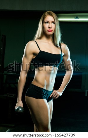 Beautiful sporty muscular woman with two dumbbells at the old gym