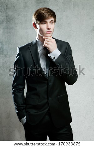 Young businessman in gray suit thinking or dreaming, on gray background
