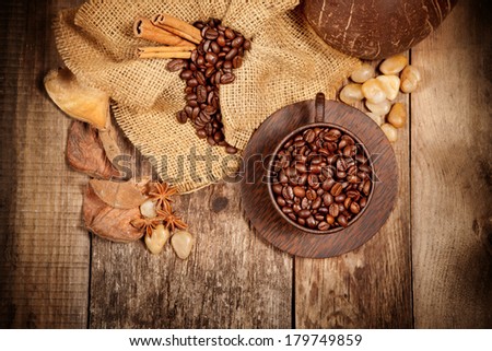 Wooden cup with coffee-beans and spicery on old wooden table. Top view.