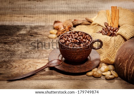 Wooden cup with coffee-beans and spicery on old wooden table