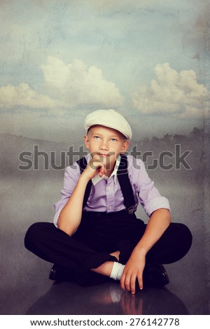 Old fashioned boy sitting and thinking or dreaming. Photo in retro style with old textured paper.