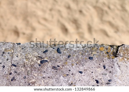Soft blurred beige sandy beach adjacent to hard concrete stone wall with rough weathered texture. Explores the concept of human versus nature, useful as a texture or background with text space.