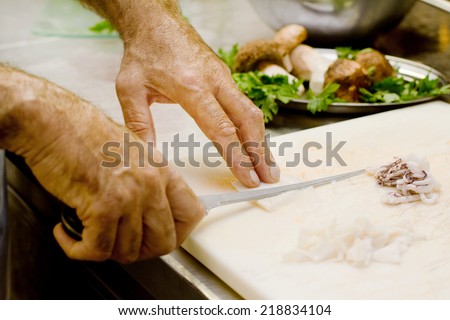 chef hands cutting small octopus against boletus background over kitchen top