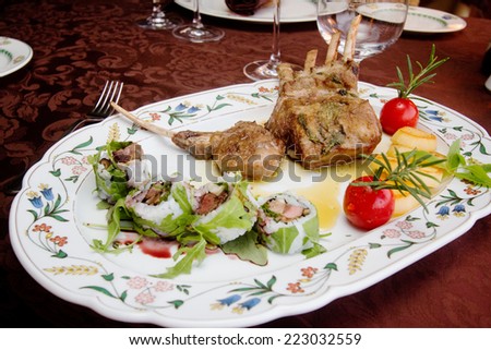 serving dish with lamb cutlet and uramaki over dressed table