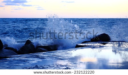 blue hour with wave crashing over dam and rocks