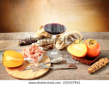 winter gourmet composition, with red wine glass, persimmon, Parma ham and decorative pumpkin
