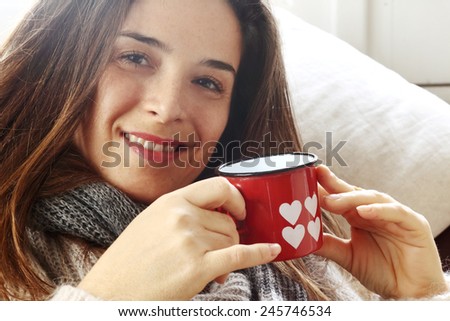 smiling girl drinking something over sofa from Valentine heart painted glass