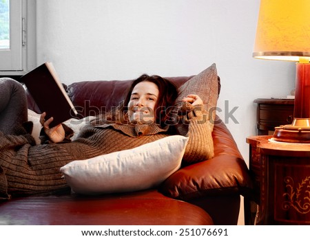 smiling girl over sofa in relax with a book with both window natural light and yellow lamp artificial light