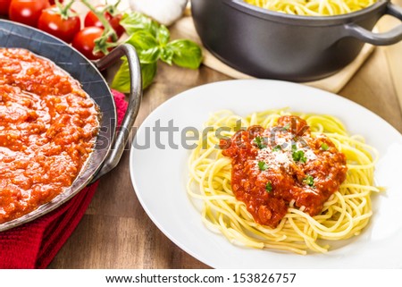 Pasta with meat sauce. Served in a pan. With tomatoes, basil and garlic in the background