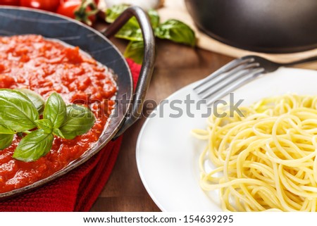 Pasta with meat sauce. Served in a pan. With tomatoes, basil and garlic in the background