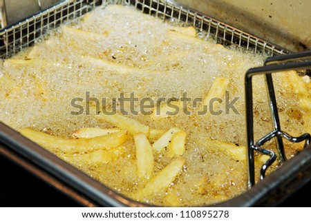 Closeup of many french fries in hot fat in a deep fryer