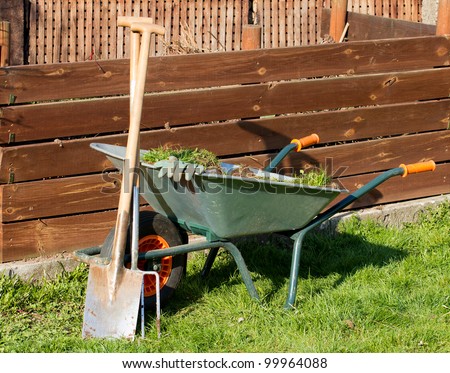 Full barrow with gloves a spade and a garden fork in front of a compost