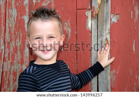 smiling young boy with spiky hair posing by an old red barn