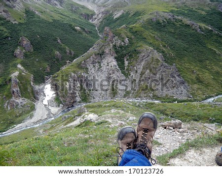 man\'s feet wearing boots hanging over mountain cliff