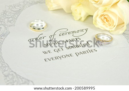 wedding rings on contemporary wedding invitation with bridal rose bouquet