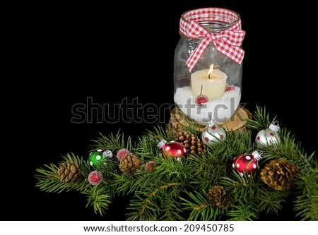 candle in mason jar with holiday ornaments and pine branch