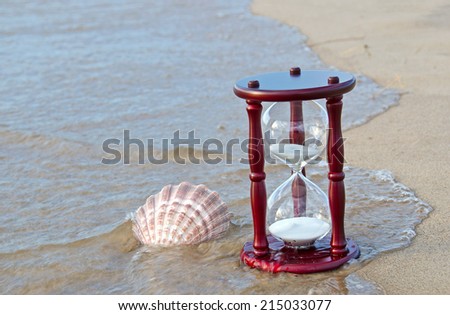 sand timer and seashell in water on the seashore