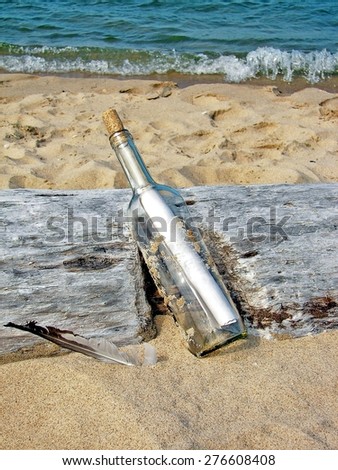 message in a bottle and seagull feather on a driftwood log on the beach