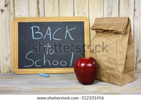 back to school sign on black chalkboard with paper sack lunch and red apple
