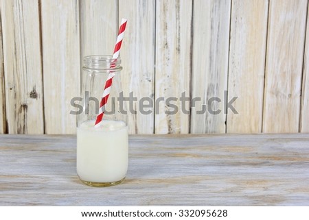 white milk in glass milk bottle with red and white striped straw on whitewashed wood