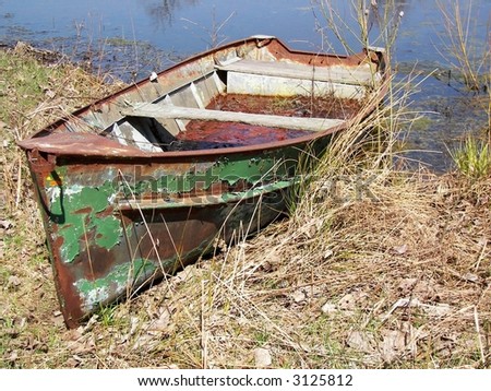 rusty old row boat with peeling green paint in weeds