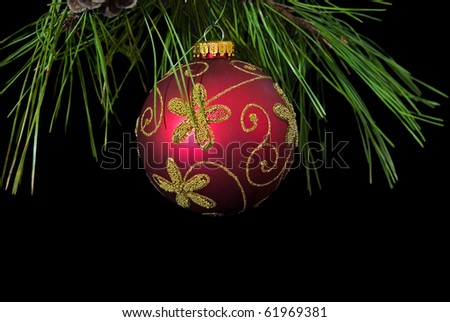 red and gold ornament hanging from pine bough