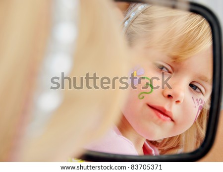 face painting on little blond girl looking in mirror