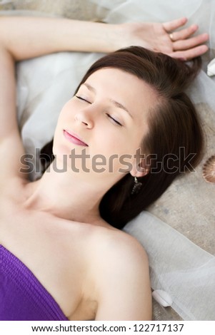 Beautiful girl is lying on fabric and sand with sea shells and being asleep