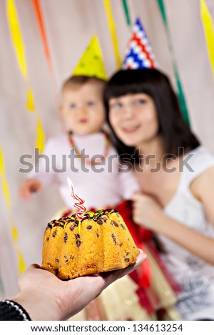 First birthday cake with one candle, mother with baby at the background
