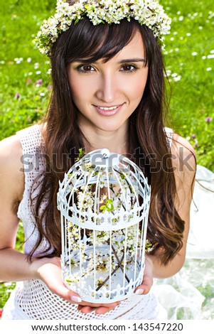 Portrait of young smiling woman in the spring garden with blossom wreath and cage