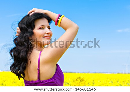 Portrait of a beautiful brunette in violet dress in oilseed rape field, freedom concept