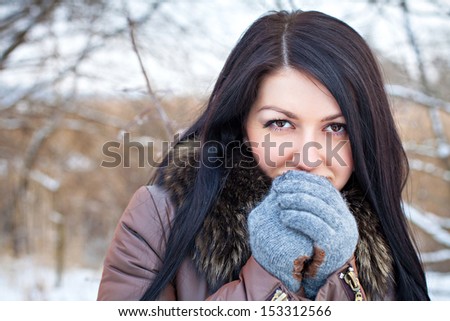 Girl in the park in winter warms the hands of breath