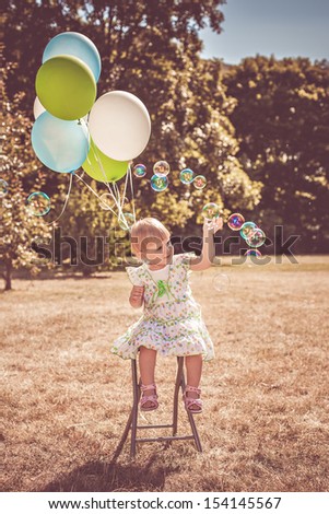 Cute girl playing in the park with soap bubbles and balloons