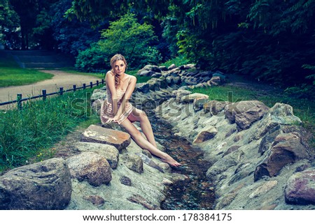 Young beautiful woman sitting on rock by stream in park