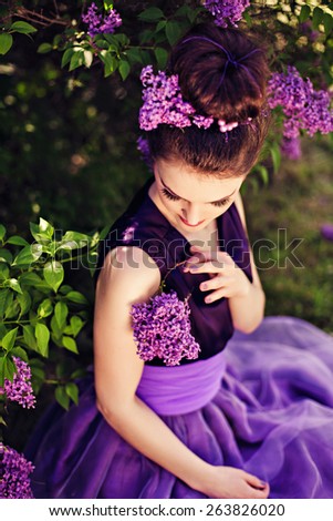 Beautiful girl in lilac ball dress among the flowers in the garden