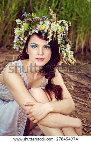 Young beautiful woman in grey dress with flower wreath at the lake