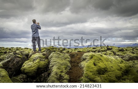 A tourist snapping a photo of moss covered lava rocks in Vatnajokull National Park, Iceland