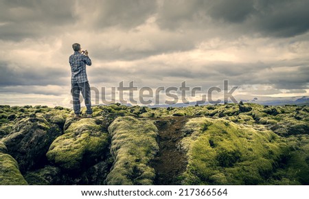A tourist snapping a photo of moss covered lava rocks in Vatnajokull National Park, Iceland