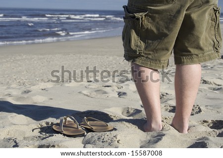 A young man stands next to his empty sandals on the beach