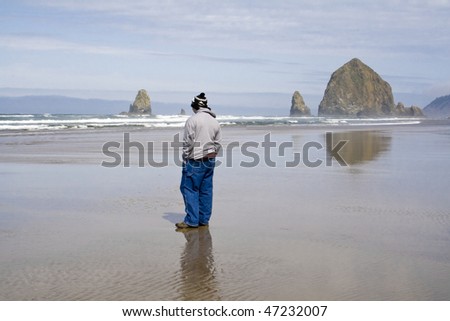 A person watches the waves crashing on Cannon Beach on a chilly but sunny day