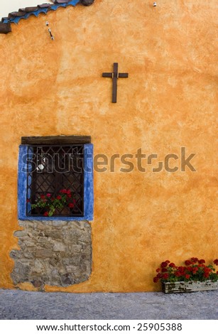 Vertical view of the  brightly colored stucco wall with a wooden cross and red flowers. Sardinia, Italy