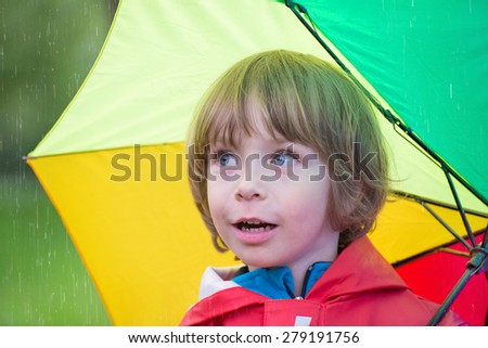Closeup of an adorable little boy with rainbow colors umbrella in the rain