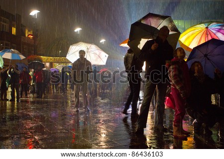 Man standing alone in a crowd when it is raining with enlightened umbrellas.