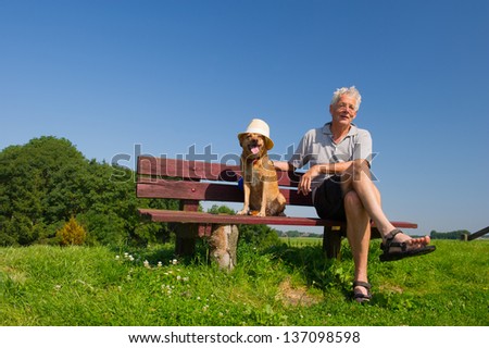 Funny wet dog with hat on bench outdoor with his owner sitting in nature landscape