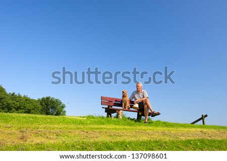 Funny wet dog with hat on bench outdoor with his owner sitting in nature landscape