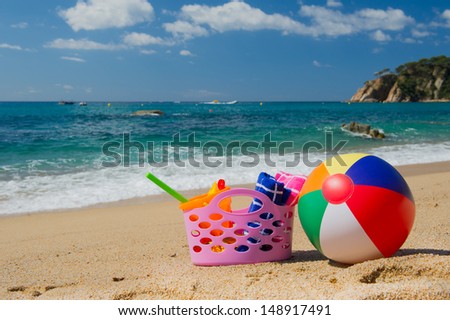 Pink beach bag and colorful ball in the sand near the water line at the Spanish beach