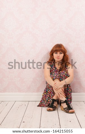 Sad woman sitting at te floor in room with vintage wall paper