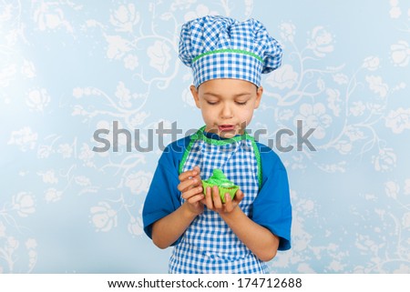 Little boy is eating his self made cupcake with vintage wall paper in background