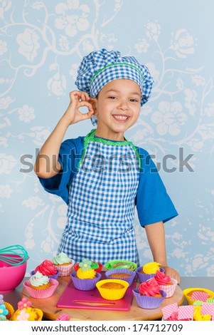 Little boy is baking colorful cupcakes with vintage wall paper in background